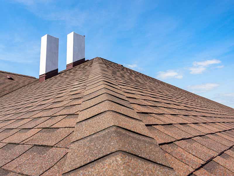 Close up of a residential roof with rust-colored shingles and two white chimneys